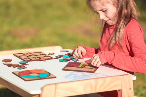 Uma criança alegre brinca alegremente ao ar livre com um jogo de tabuleiro em cima de uma mesa. Ótima ideia para atividades ao ar livre